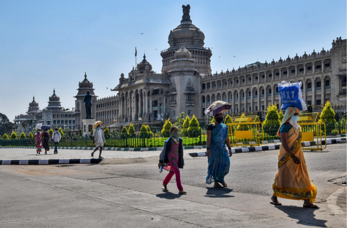 Image with people walking in a line, with bags on their head, wearing COVID-19 masks